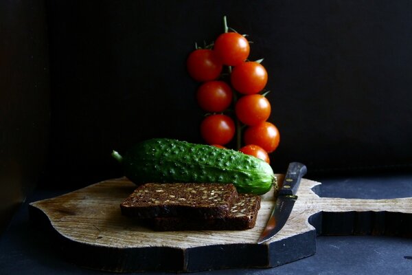 Bread and cucumbers are waiting for a knife on the board