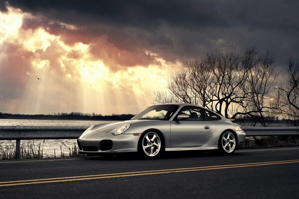 Une Porsche d argent se tient à côté de l eau sous les nuages