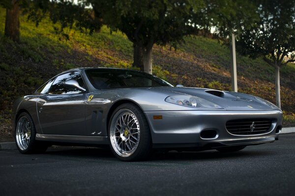 Серебристый Ferrari 575 maranello среди деревьев