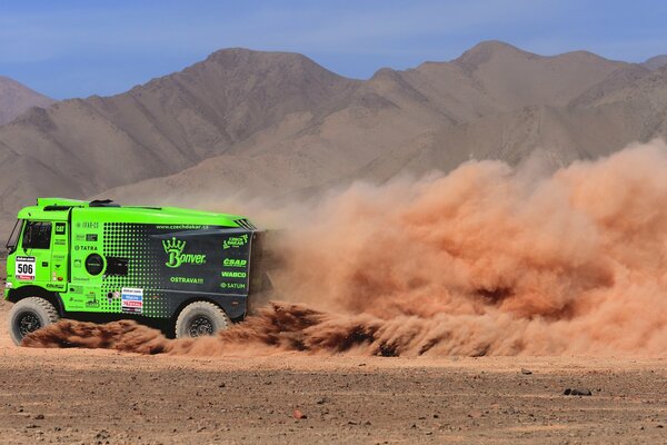 A green truck drives at high speed through the desert