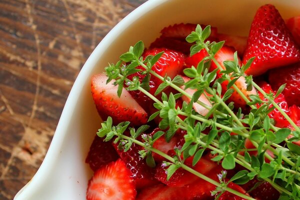 Fresas en un tazón blanco con ramitas de hierba