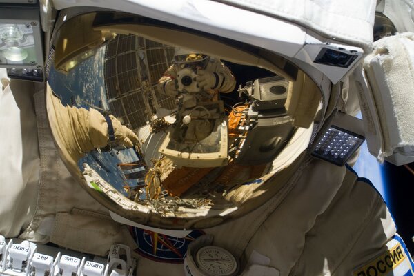 Two astronauts are photographed in space through the reflection on the helmet of the spacesuit