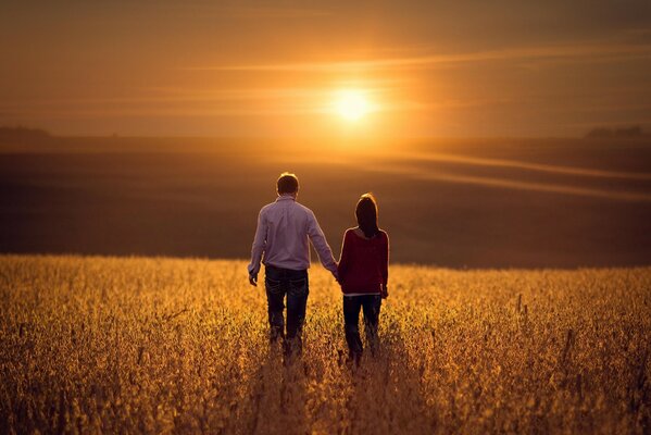 Ein Liebespaar geht auf dem Feld vor dem Hintergrund des Sonnenuntergangs spazieren