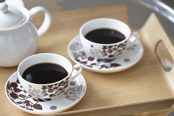 Two white cups in a floral pattern with coffee