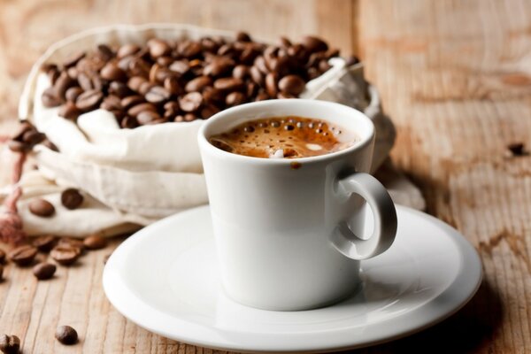 On a wooden table there is a white mug with coffee and a bag of coffee beans