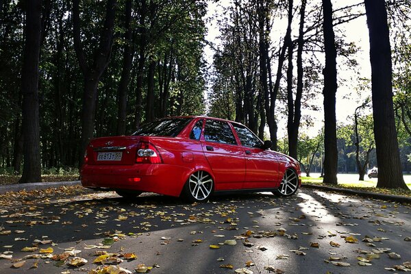 Prior s red Lada on the road with autumn foliage