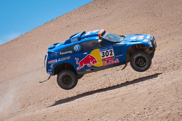 Une Volkswagen Touareg bleue dans les airs et dans le désert au rallye