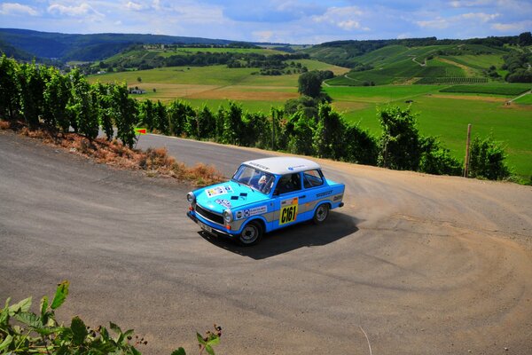 Une voiture rare bleue roule sur une route de montagne sur un fond de collines verdoyantes