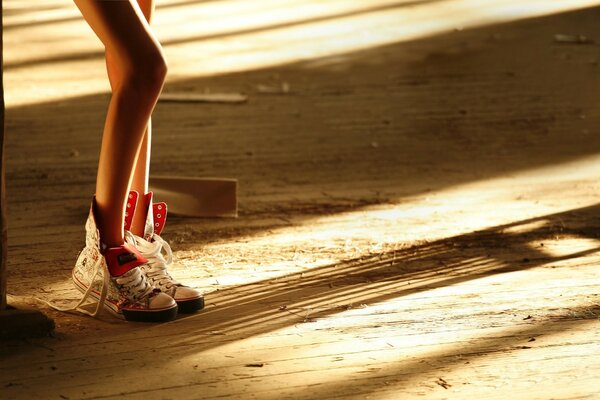 Slender legs in unlaced sneakers on the plank floor