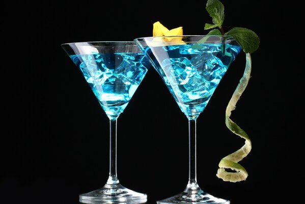 Sur un fond noir, il y a 2 verres à Martini avec un liquide bleu