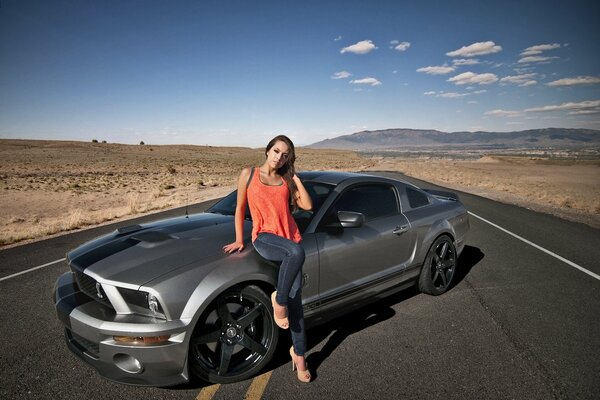 Schönes Mädchen in einem orangefarbenen Top neben dem Mustang Ji Ti 500 in der Wüste