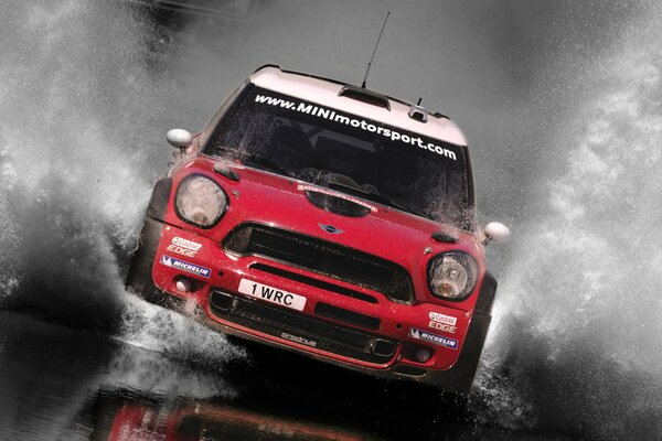 A red mini Cooper car drives through a huge puddle