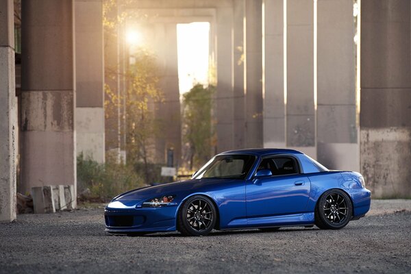 A blue Honda. Beautiful photo with the sun in the parking lot under the bridge