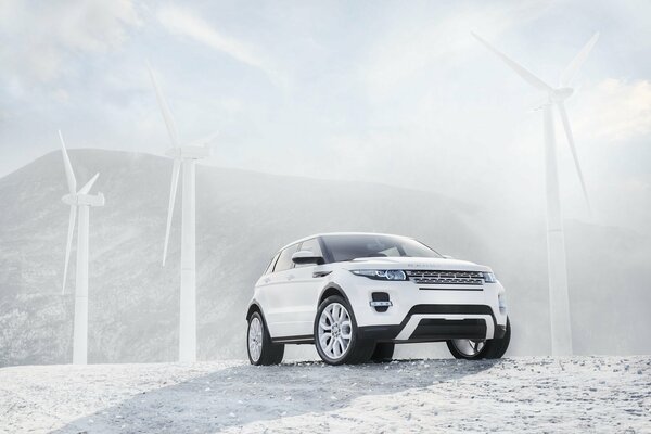 White Range Rover on the background of white wind turbines, mountains and clear sky