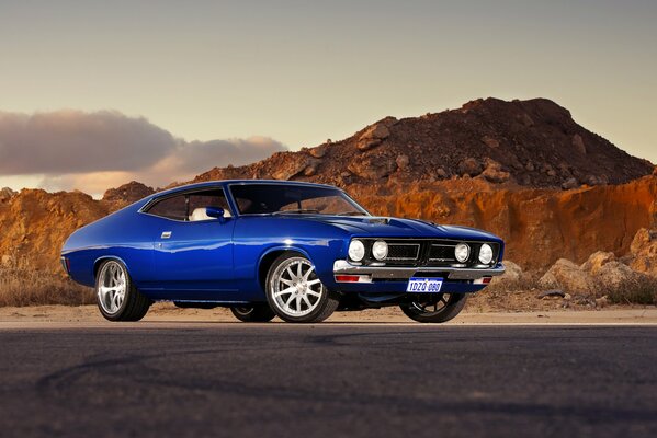 Voiture bleue Ford sur fond de montagnes et ciel nuageux