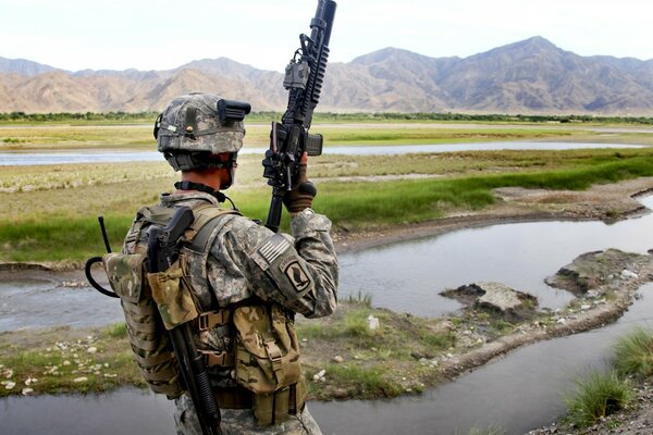 A soldier stands with a machine gun against the background of the river