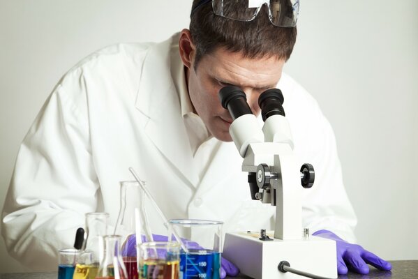 Scienziato in camice bianco e guanti che guarda al microscopio