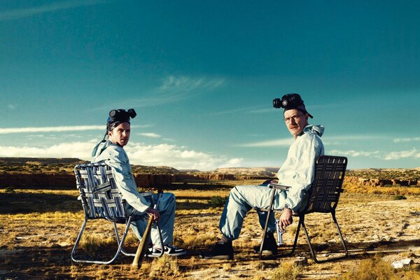 Two men in strange clothes are sitting in the desert