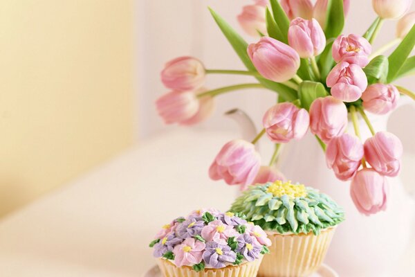 Zarte Cupcakes stehen auf einem Tisch mit einem Blumenstrauß aus Tulpen in einer Vase