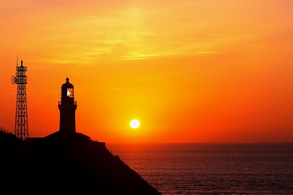 Faro en el fondo de la puesta de sol en el océano