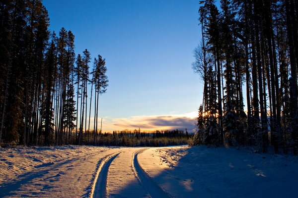 Verschneite Straße bei Sonnenuntergang im Winterwald