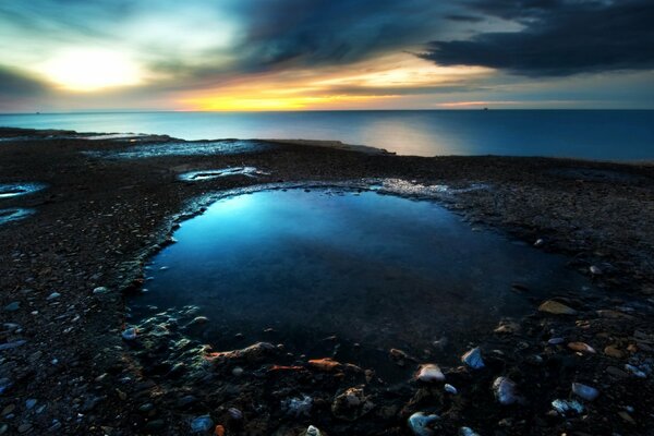 Der felsige Strand und das blaue Meer bei den letzten Sonnenstrahlen des Sonnenuntergangs