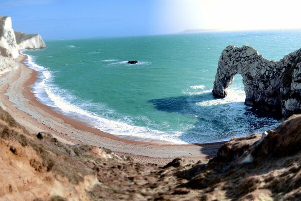 Laguna, playa salvaje y océano azul con un arco de surf en relieve en la roca