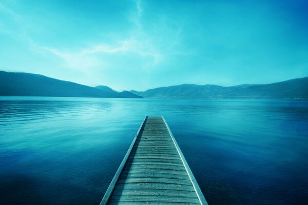 Мостик в озере напротив гор в голубых тонах