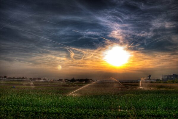 View of watering in a field with clouds and sun