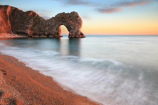 The beach and the rock drowning in the sea at sunset