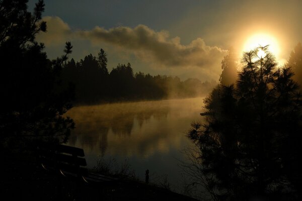 A bench by the river and a beautiful sky with the sun