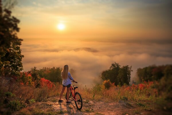 A girl with a bicycle stands in front of a beautiful landscape