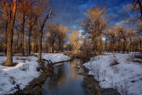 Winter landscape. A river in the middle of the forest and snow on the banks