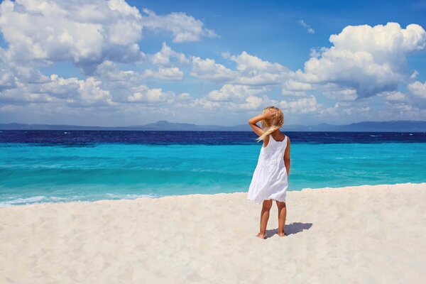 Image of a girl in a white dress on the beach near the blue sea