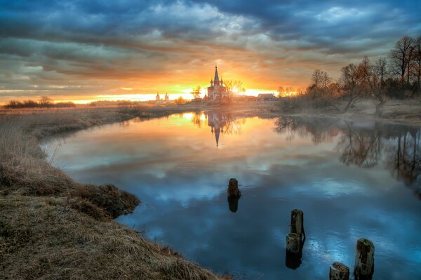 Kirche vor dem Teich vor dem Hintergrund der orangefarbenen Morgendämmerung