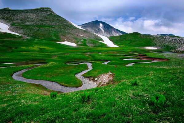 Panorama de montaña con un río sinuoso y hierba verde