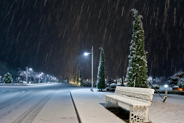 Śnieg w nocnym mieście na tle jasnych latarni