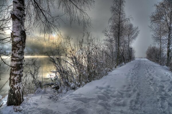 Camino cubierto de nieve junto al río al atardecer