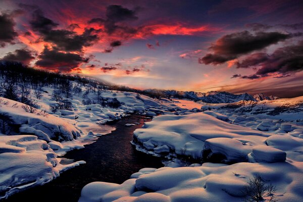 Wintermorgendämmerung in den Bergen ein Fluss, der sich durch den Schnee schleicht