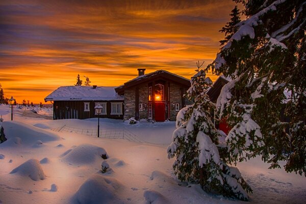 Ein cool abgebildeter Sonnenuntergang ist schön. Die Landschaft umfasst ein Haus mit Schnee Himmel, die in Winterfarben gekleidet sind. die Natur leuchtet herrlich und verwandelt den weißen Schnee in eine Fortsetzung des orangefarbenen Himmels