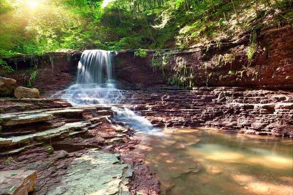 Stone waterfall in the forest in the rays of the sun