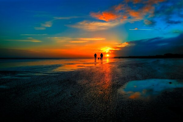 People walk along the shore at sunset