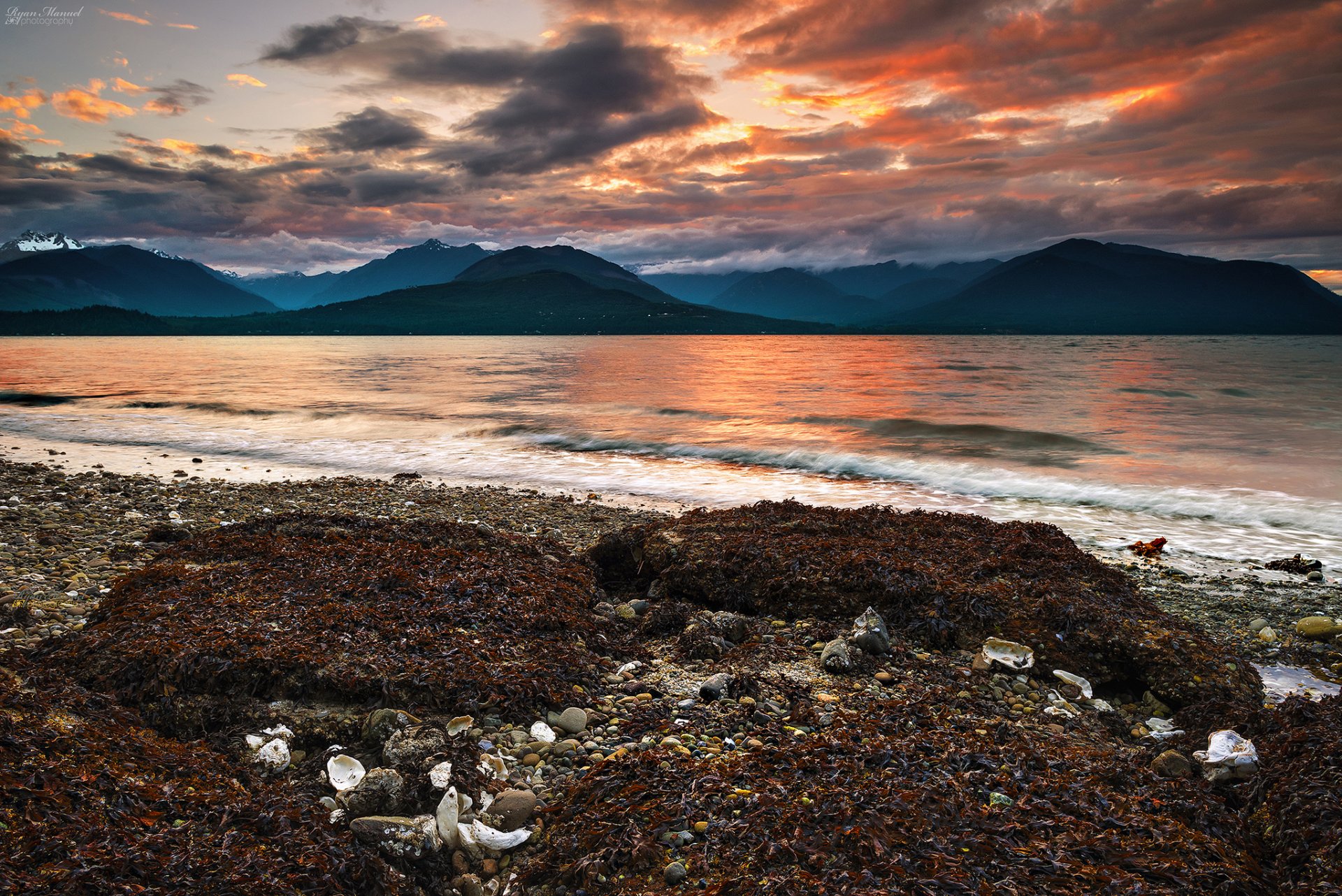 montagnes plage cailloux algues mer coucher de soleil