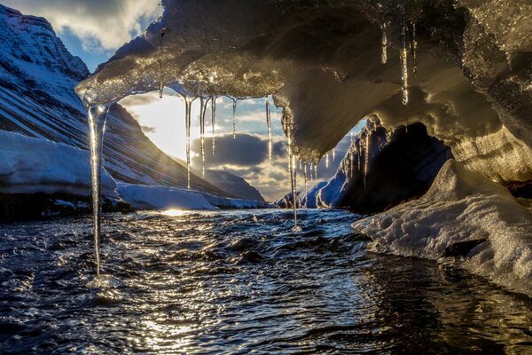 Icicles hang over the river against the background of the sun