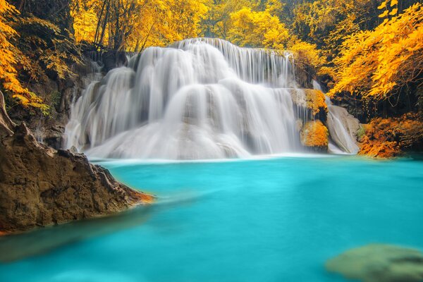 Paisaje otoñal de una cascada en un lago azul rodeado de un bosque amarillo