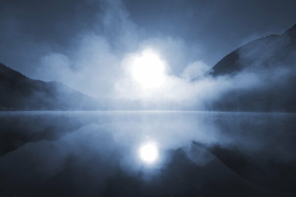 In the fog, the sun is reflected in the lake