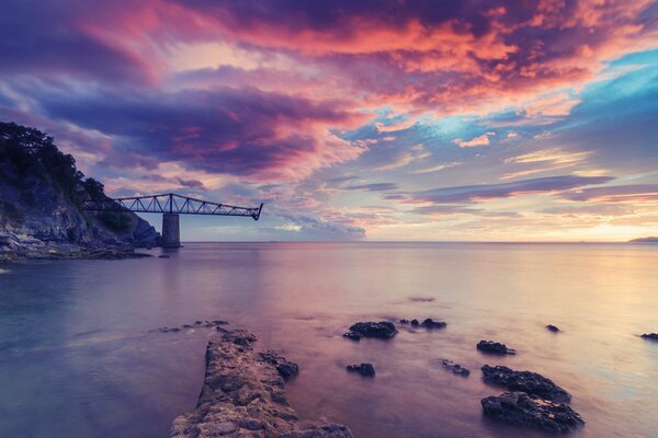 The wreckage of a bridge in the ocean in the color of a pink sunset sky