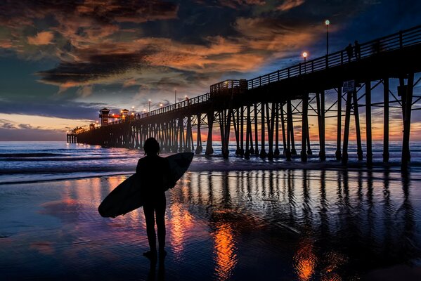 Night surfing, a girl is waiting for the tide at the pier
