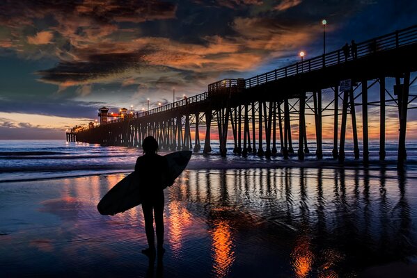 Surf nocturno, chica esperando la marea en el muelle