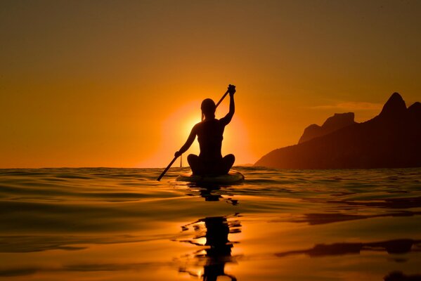 Silhouette di una ragazza nei raggi del tramonto su un kayak